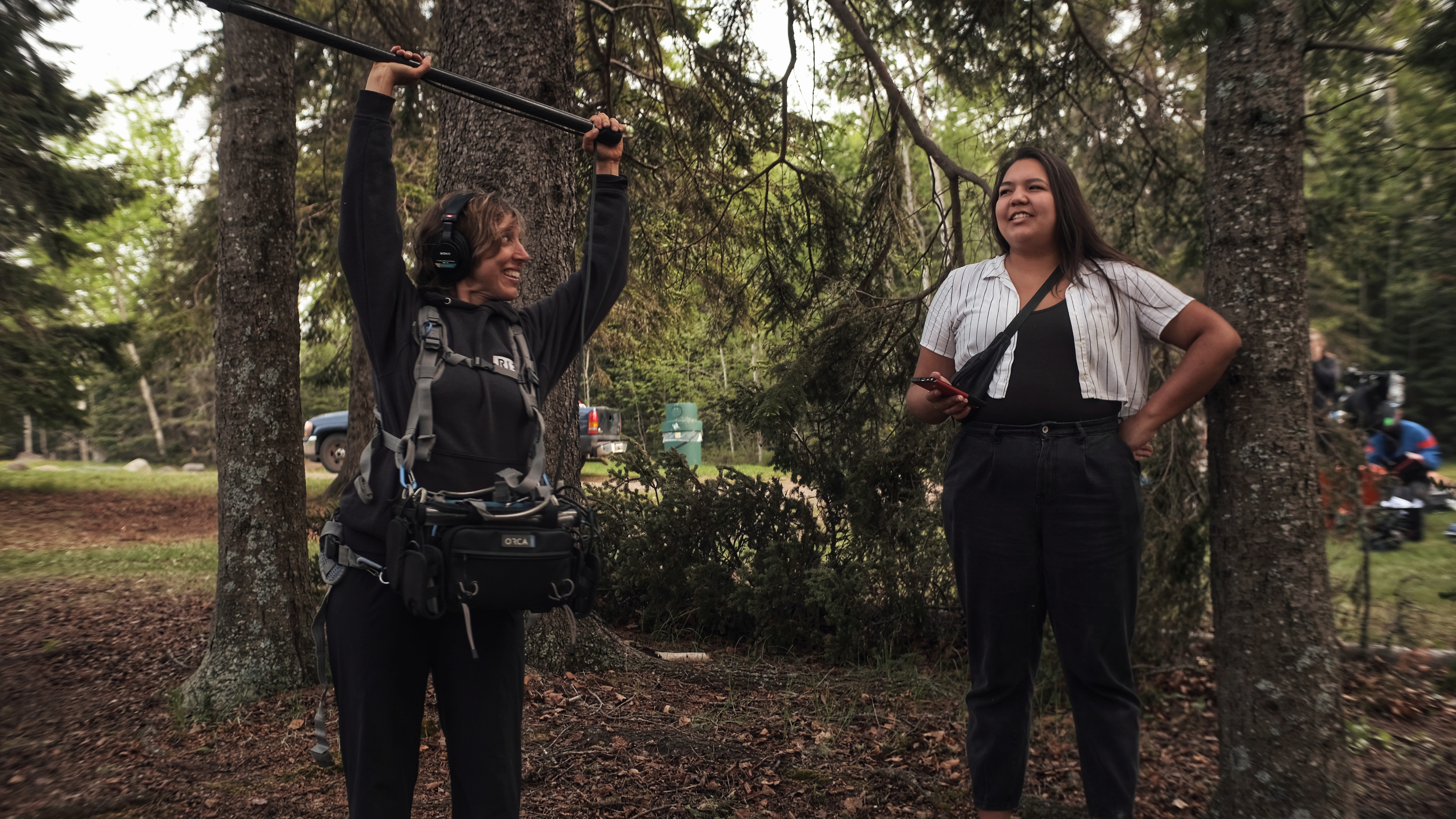 Two people smiling while creating a film. One holds a microphone boom.