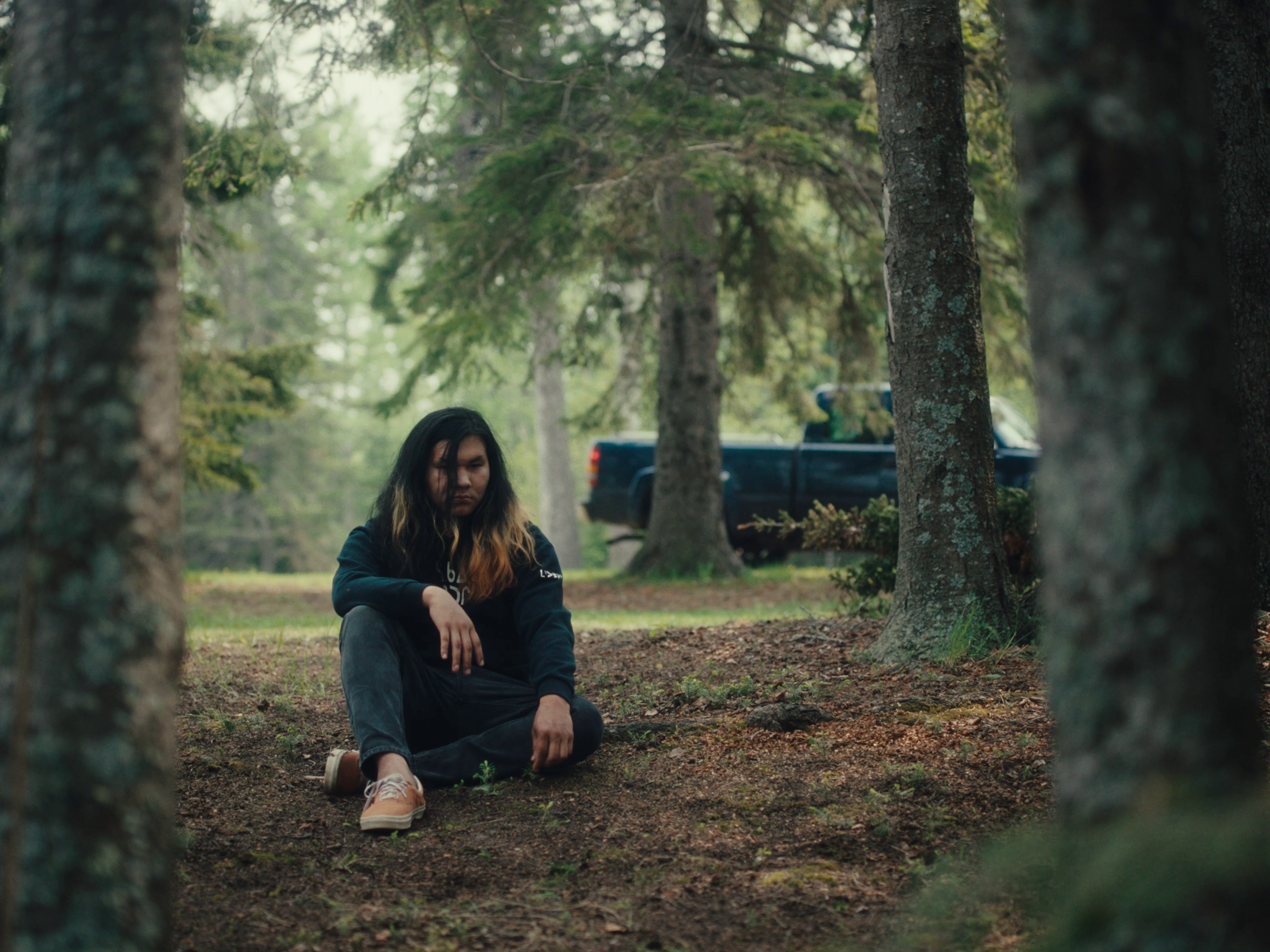 A person sitting in the wilderness with a  truck behind them.