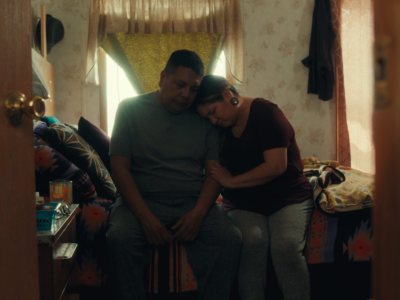 Two people sitting on a bed inside their house. 